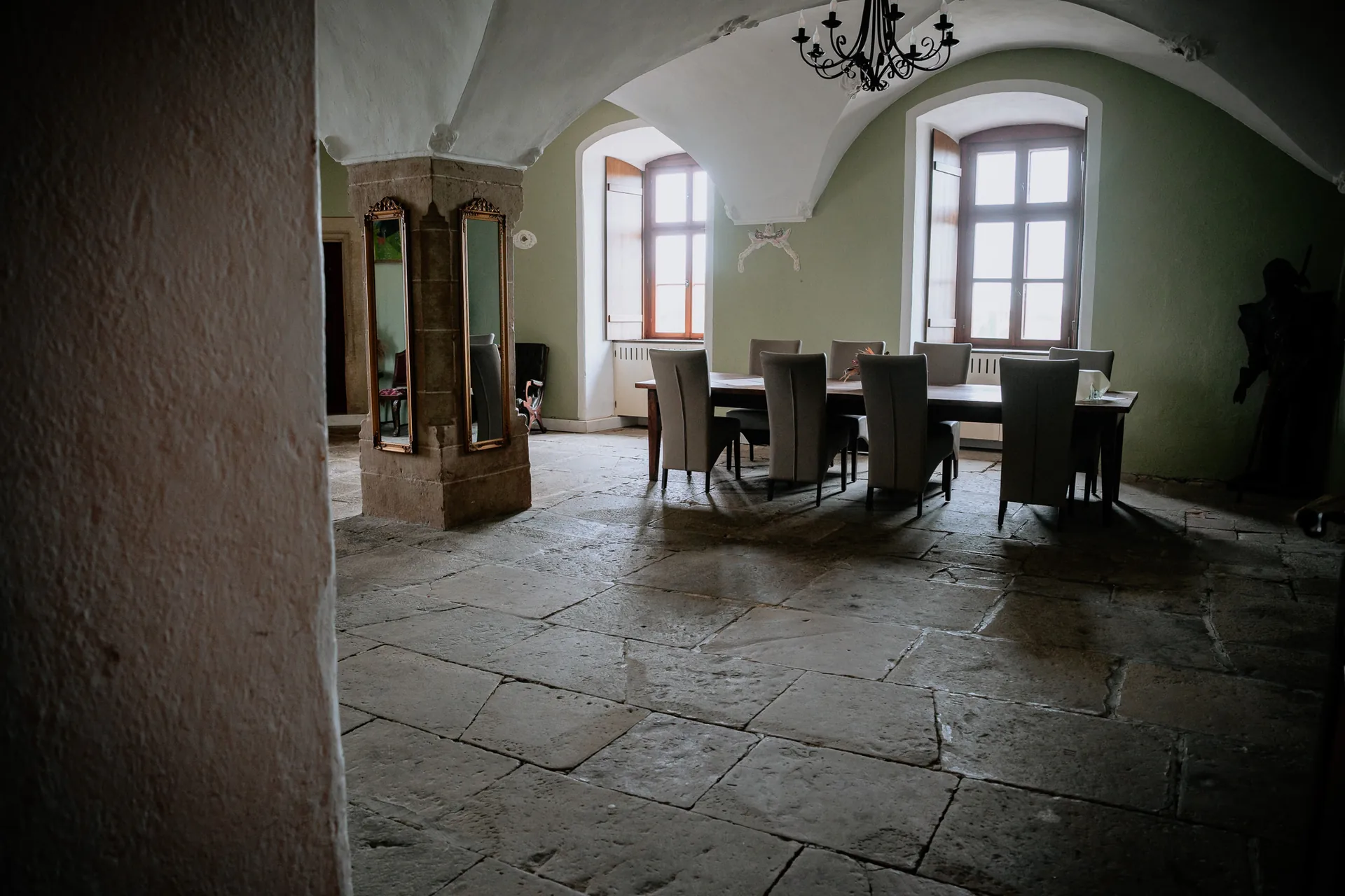 Bräutigamraum mit Steinpfeiler, Standspiegeln und langer Tafel vor grünen Wänden