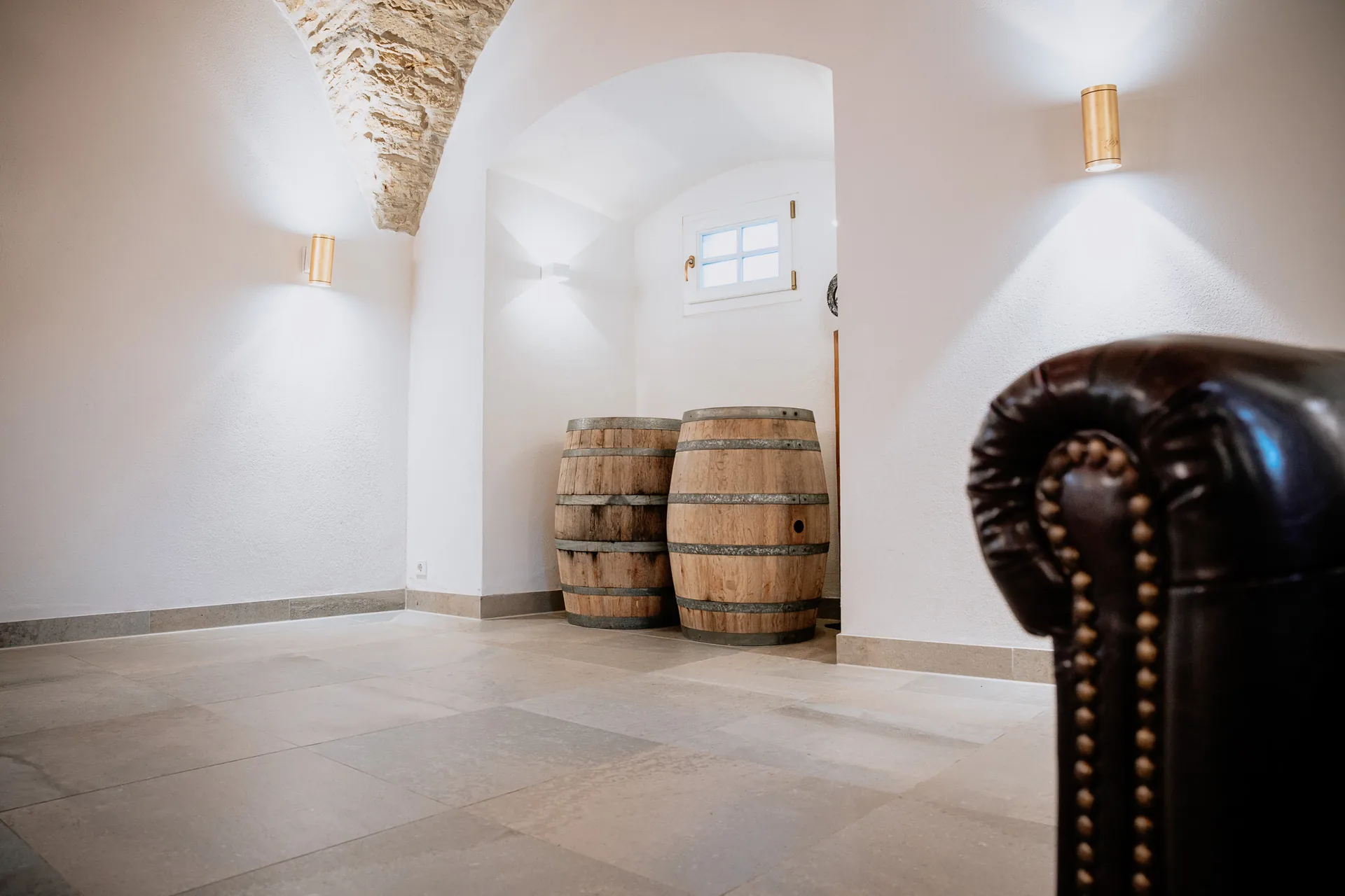 Gewölbenische im Foyer mit zwei Holzfässern, Wandleuchten und Chesterfield-Sessel im Vordergrund