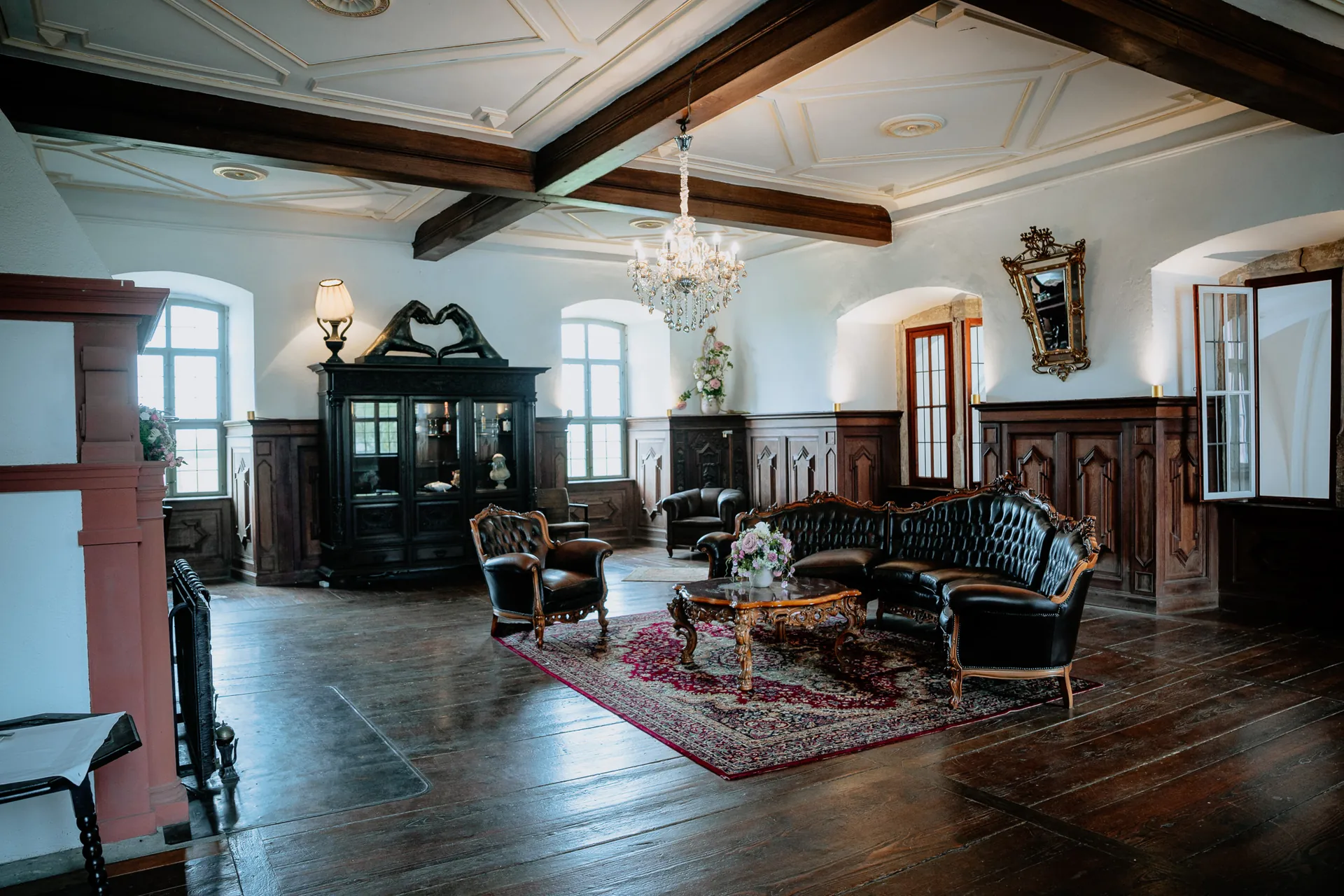 Brautraum mit Kassettendecke, Kronleuchter, historischer Holzvertäfelung und lederner Sitzgruppe