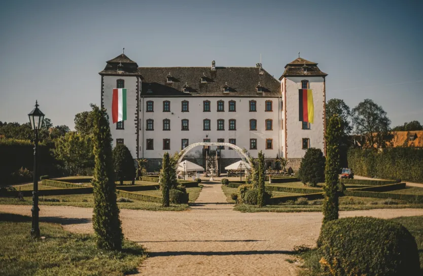 Schlossfassade mit zwei Flaggen an den Türmen und Blick durch die Parkallee