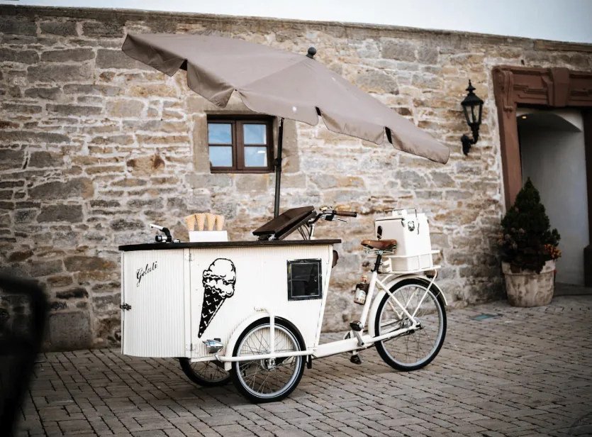 Weißes Eisfahrrad mit Sonnenschirm vor der Natursteinmauer im Schlosshof