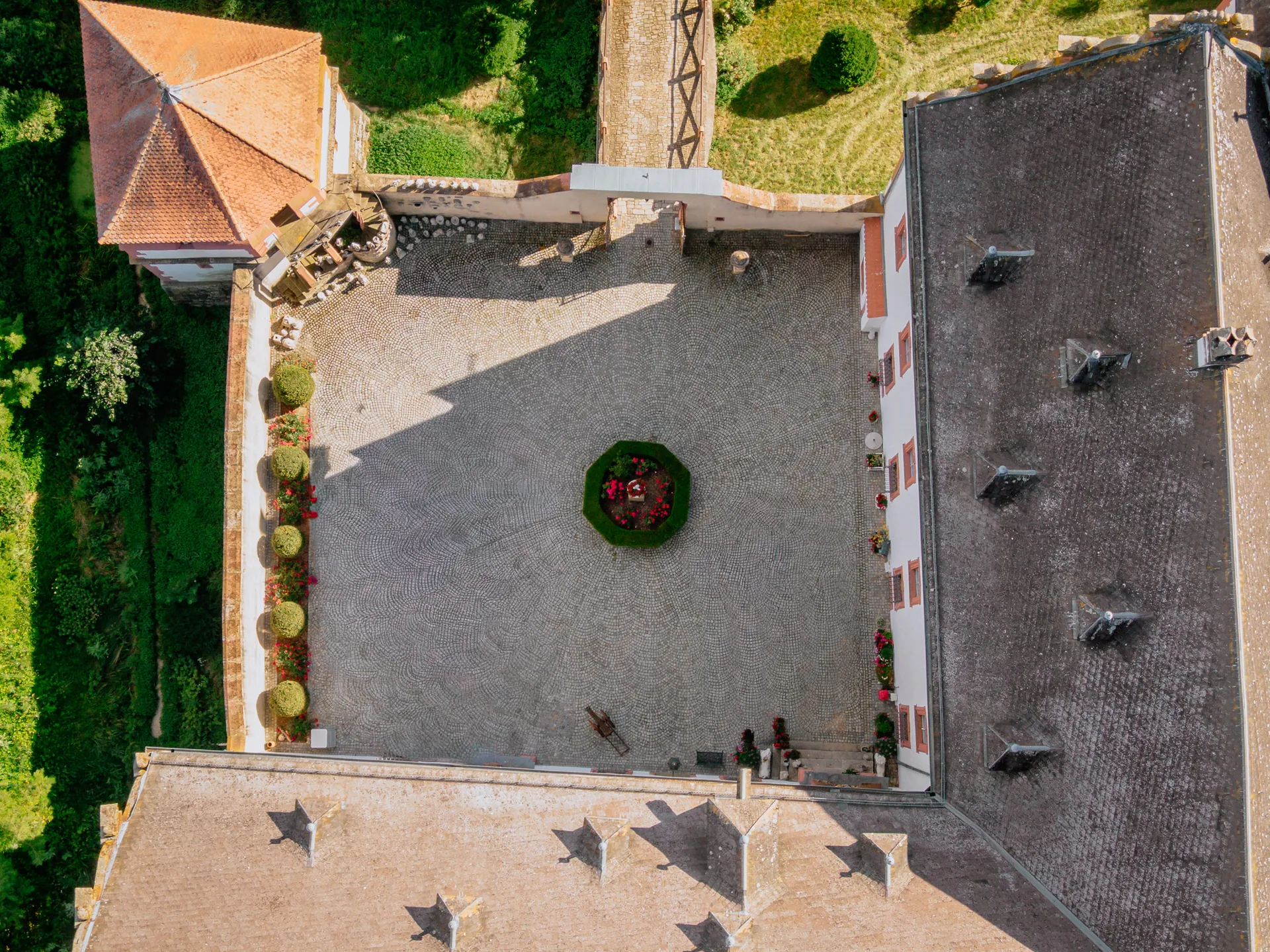 Luftaufnahme des gepflasterten Schlosshofs mit rundem Blumenbeet, Formschnitthecken und Schlossdächern
