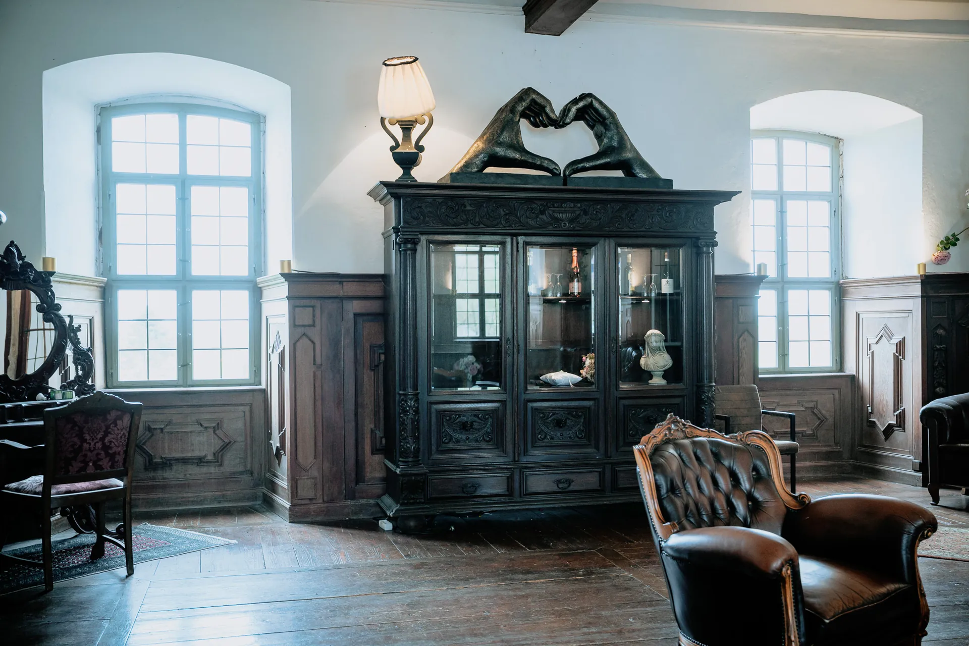 Brautraum mit schwarzer Vitrine, Kristallleuchter und lederner Sitzgruppe auf Orientteppich