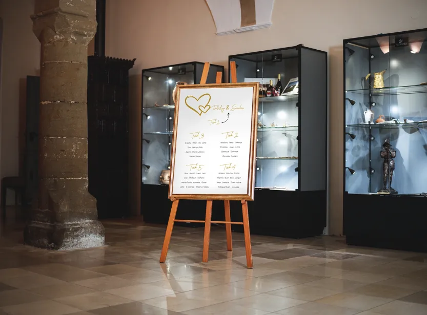 Holzstaffelei mit Sitzplan im Foyer neben Sandsteinsäule und Vitrinen