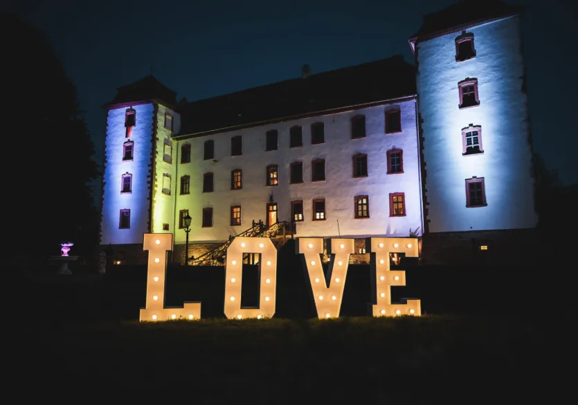 Beleuchtete LOVE-Buchstaben vor der angestrahlten Schlossfassade bei Nacht