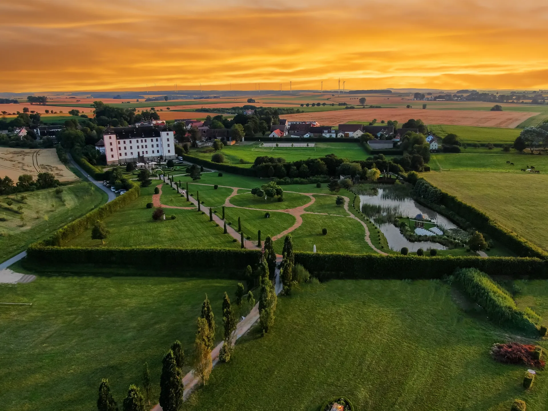 Schloss Walkershofen mit Schlosspark, geschnittenen Hecken und See aus der Luft im Abendlicht